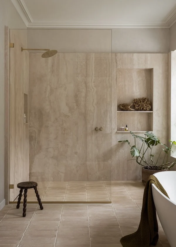Curbless walk-in shower with travertine slab walls, a single frameless glass panel, brass rain head and terracotta tile floor running straight into the shower, Georgetown